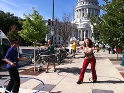 A group of adults hoola-hooping on the sidewalk near the Madison, WI state capitol building on a sunny day