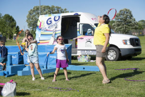 Several kids and adults twirling ribbons in front of the Fit2Go van in a field of grass