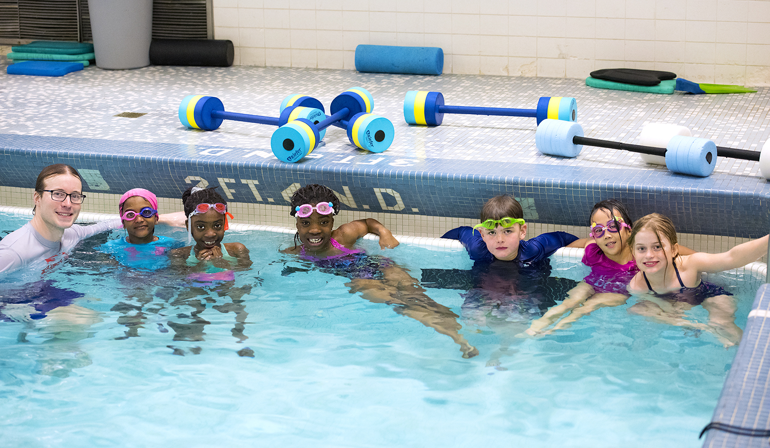 A group of students in an indoor pool with their swimming teacher