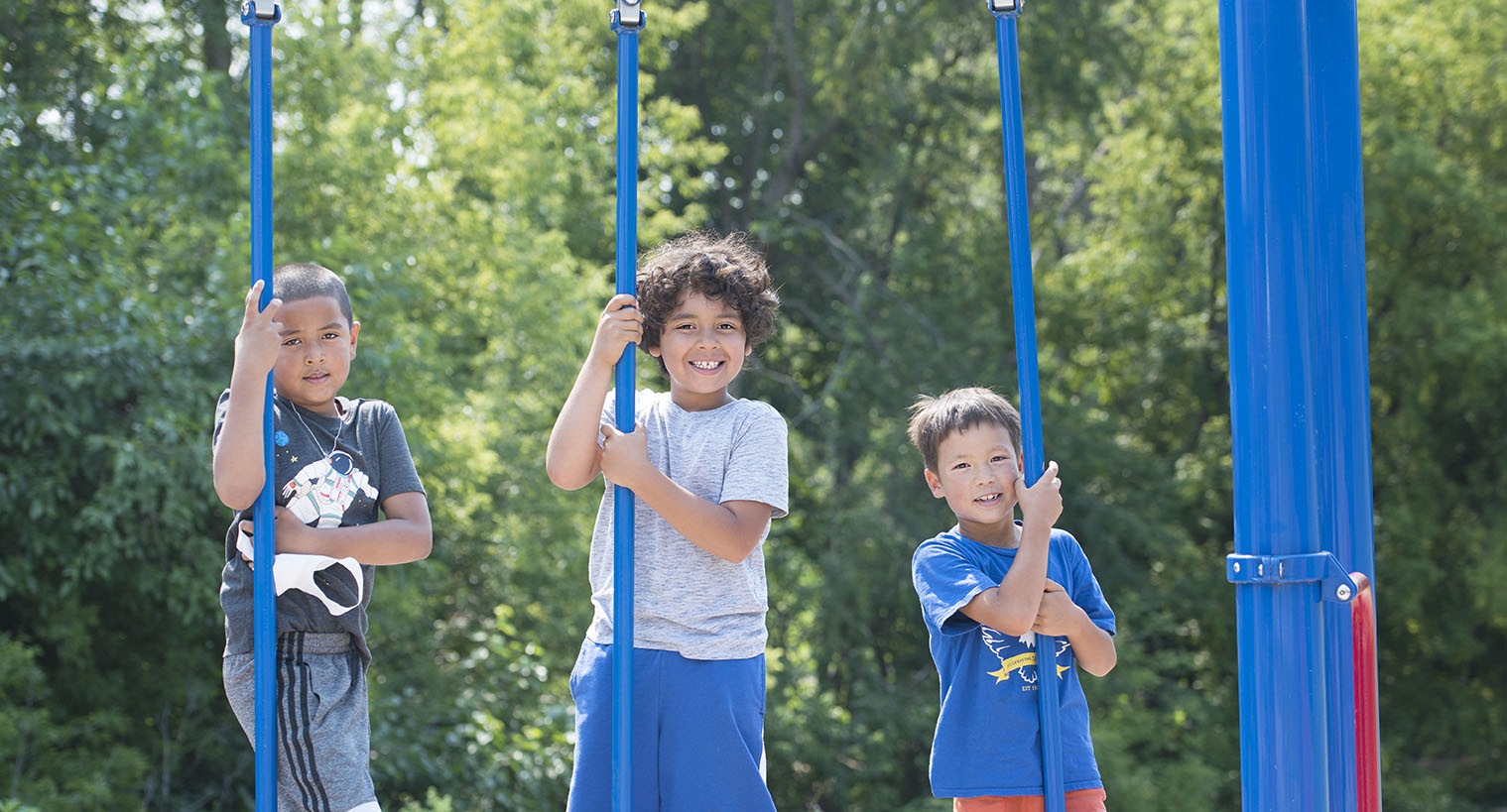 Three children playing on equipment on a playground on a sunny day