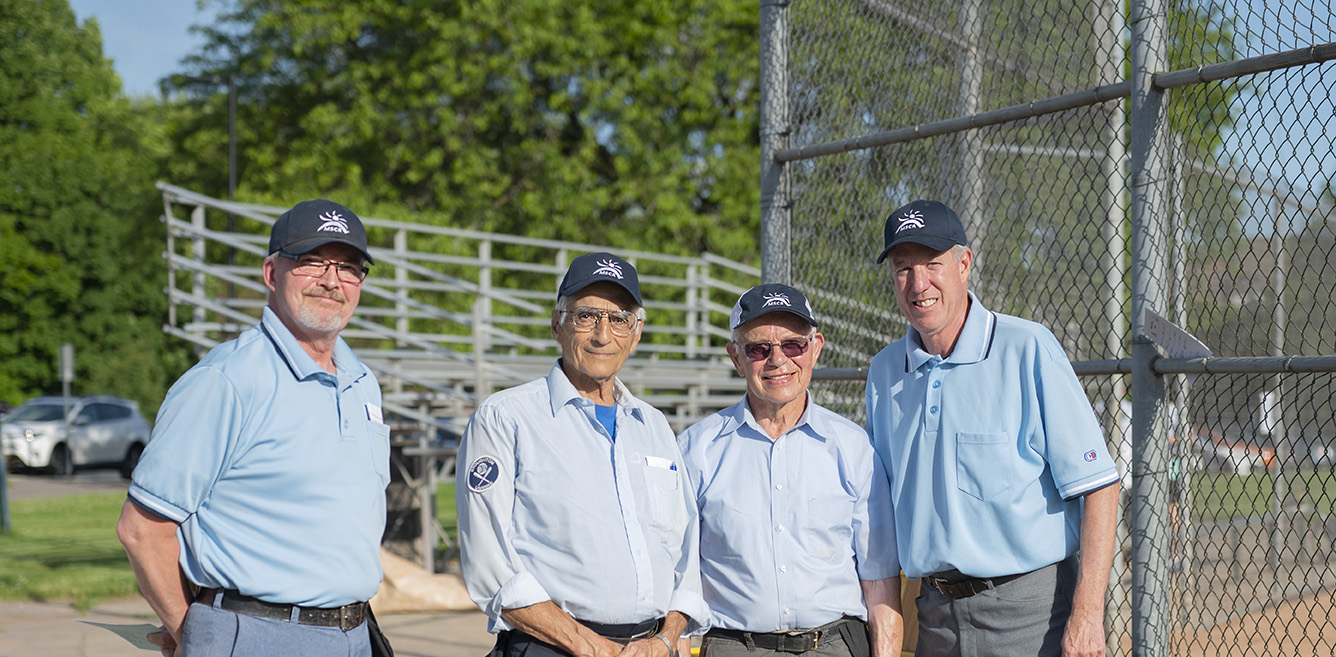 Four older men posing behind a baseball diamond