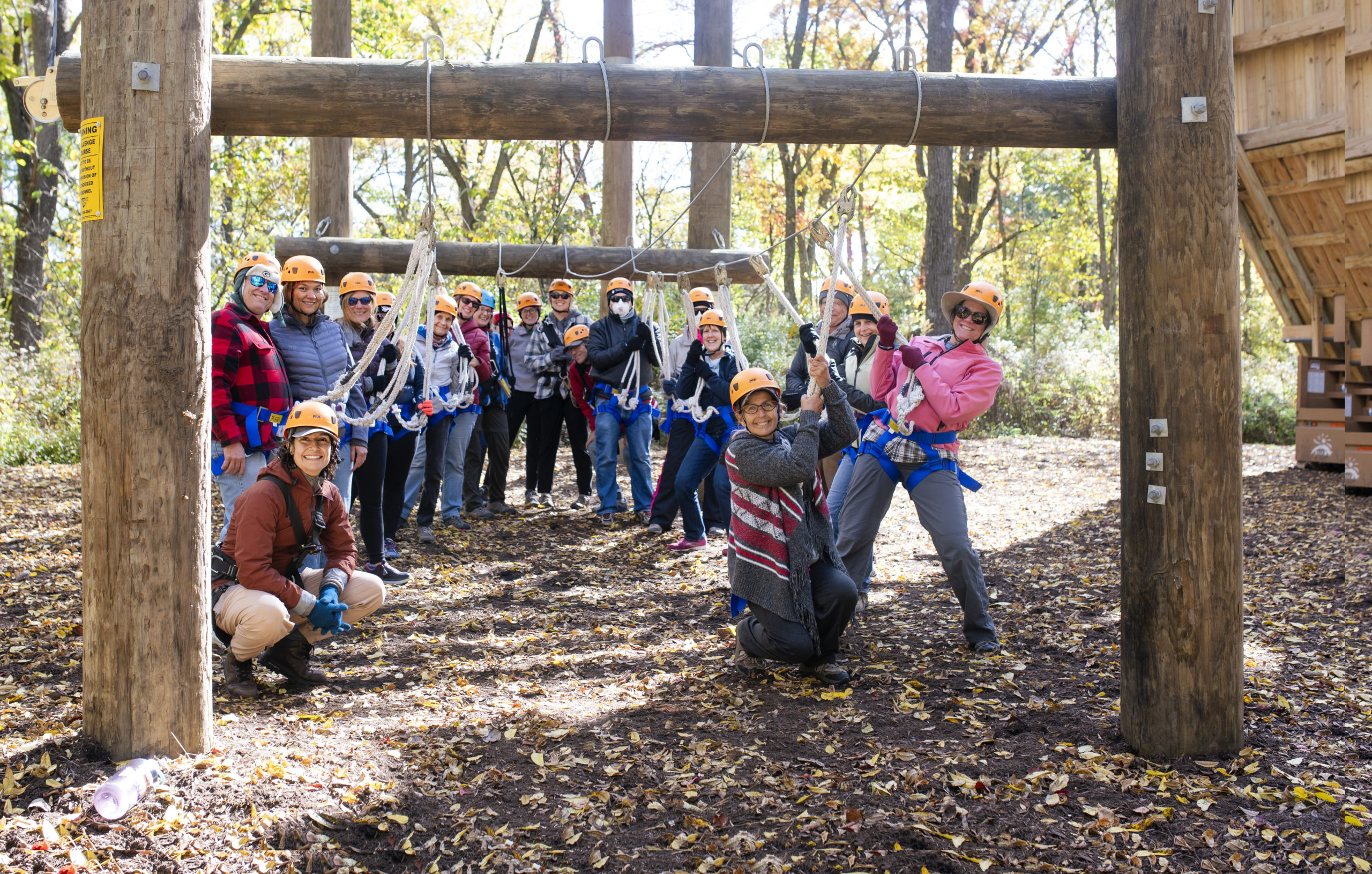 A group of people smile for the camera under a ropes course in the woods.