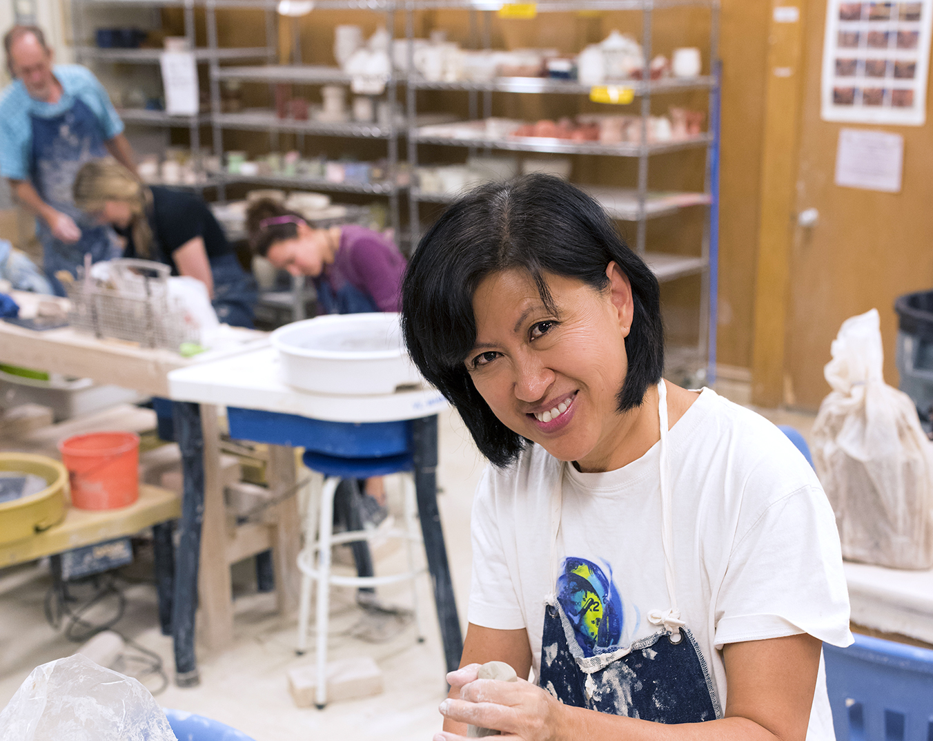An Asian-American woman in a pottery studio with other people working on a piece of clay