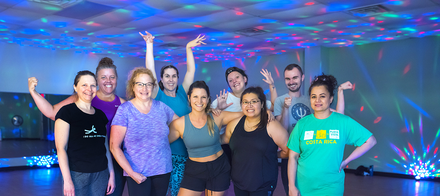 A group of adults posing in an exercise room with lots of laser lights