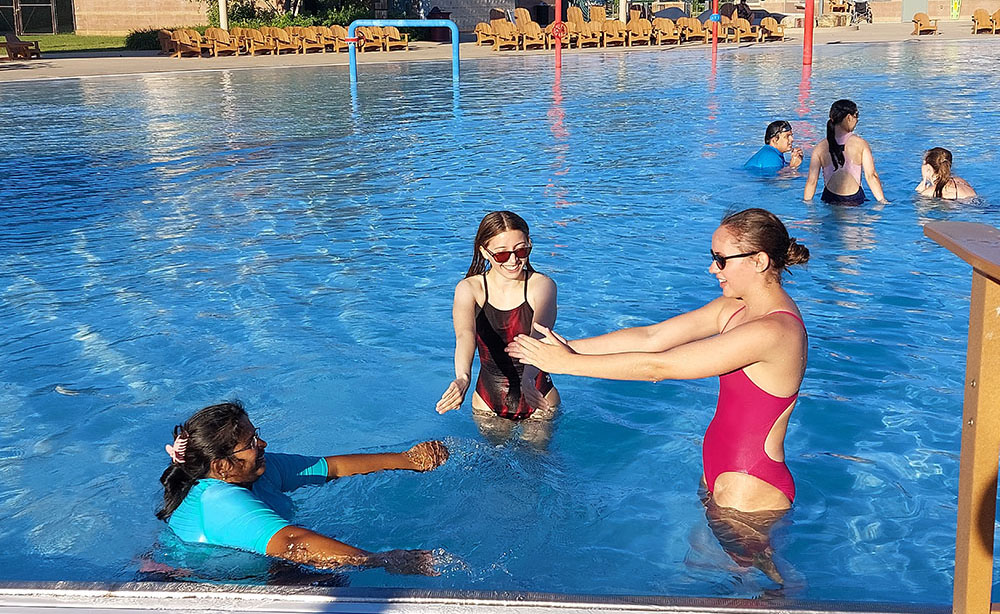 Three people in bathing suits in the Goodman Pool on a sunny day