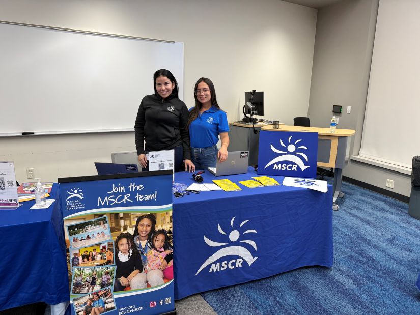 Staff standing and smiling behind a table at a job fair