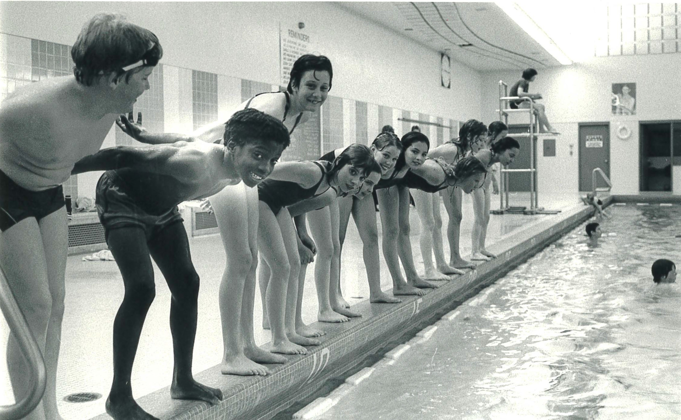 Children on the side of a pool waiting to dive in.